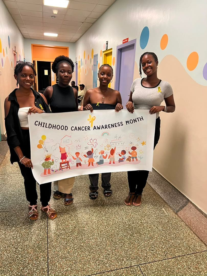Four volunteers holding a hand-drawn Childhood Cancer Awareness Month banner in a hospital corridor